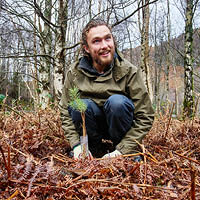 Student smiling up at the camera while planting a tree in the ground at Glen Nevis