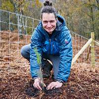 Student smiling directly at camera while planting tree in the ground