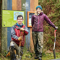 Two students smiling towards hte camera with shovels ready for tree planting