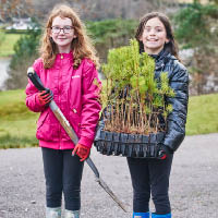 two primary school children carrying a shovel and small trees to be planted