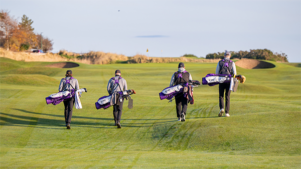 4 male golfers carryng golf bags with their backs to the camera walking on a golf course