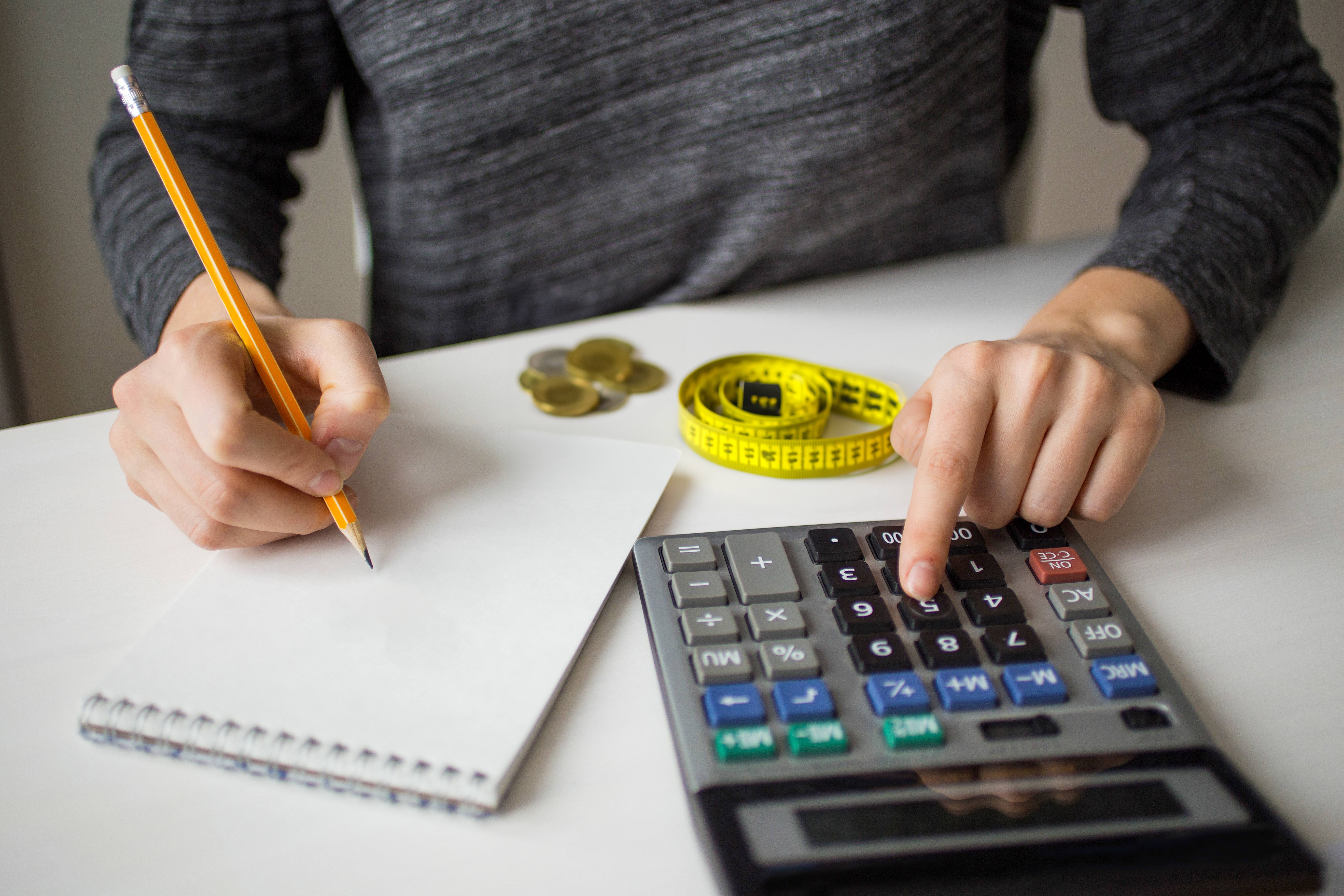 person using a calculator with a notepad and pen