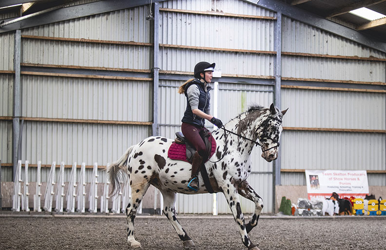 student riding horse in an indoor arena