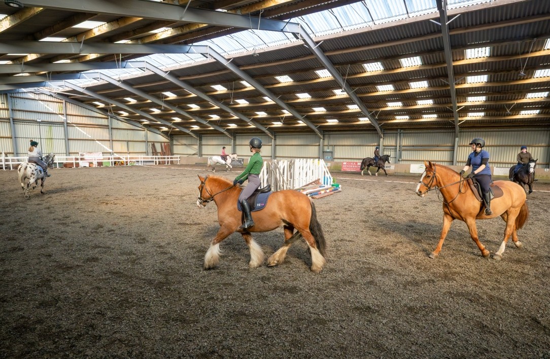 Equestrian students riding horses inside a large indoor arena Equestrian students riding horses inside a large indoor arena