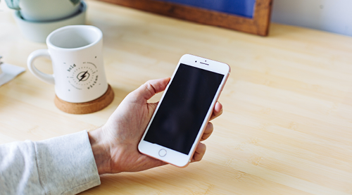 Image of person holding iPhone with a desk and mug in the background