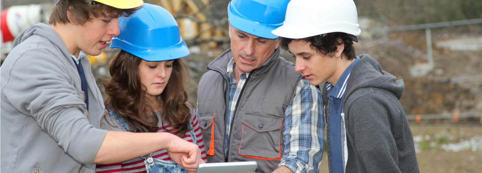 Lecturer and construction students wearing hard hats look at plans