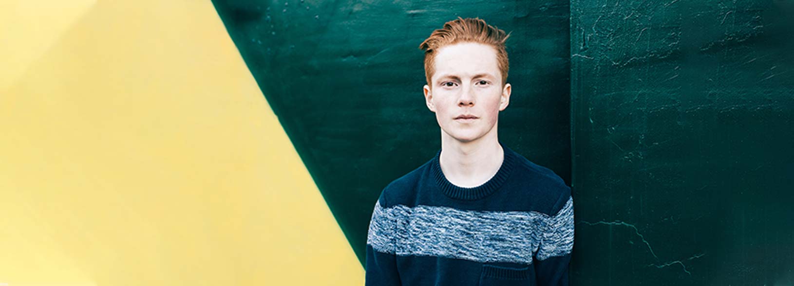 Young male student standing against dark green and yellow wall